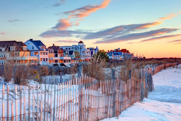 Sunset view of a beachside town with sand dunes and wooden fences.