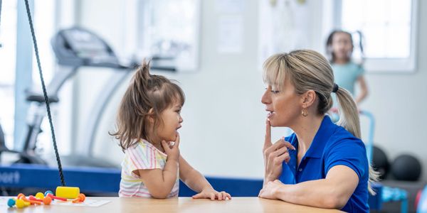Therapist and child practicing speech therapy together at a table.