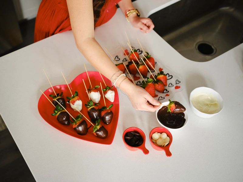 A hispanic family making chocolate dipped strawberries in a home kitchen.