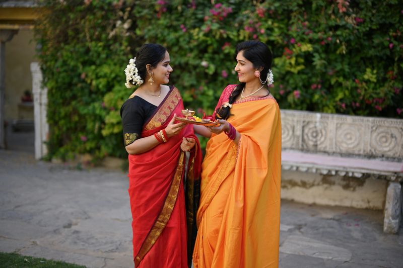 Two beautiful Indian women in saris holding a pooja plate and talking to each other in a palace in Rajasthan
