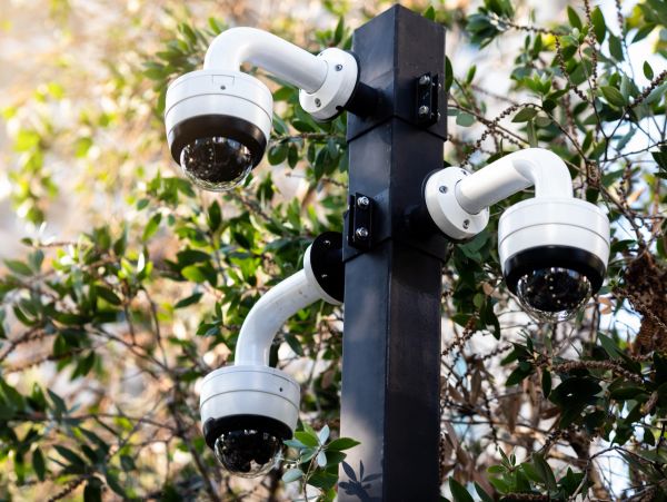 Three white security cameras on a black pole.
