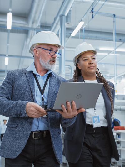 Two engineers wearing hard hats reviewing data on a laptop.
