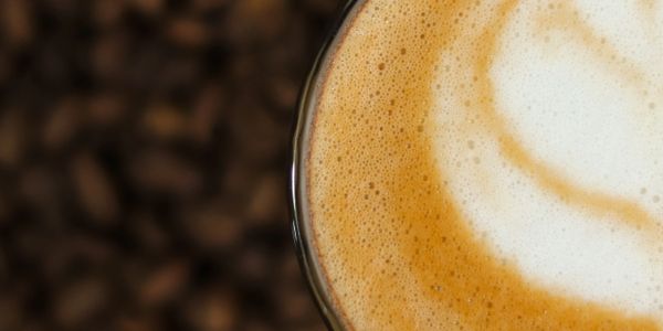 Close-up of a frothy cappuccino with coffee beans blurred in the background.