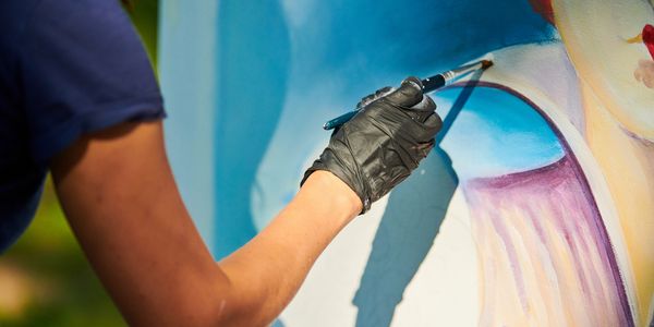 Artist painting a colorful portrait with a brush while wearing a black glove.
