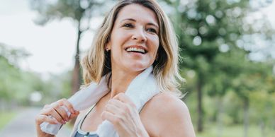 Woman smiling outdoors with towel around neck.