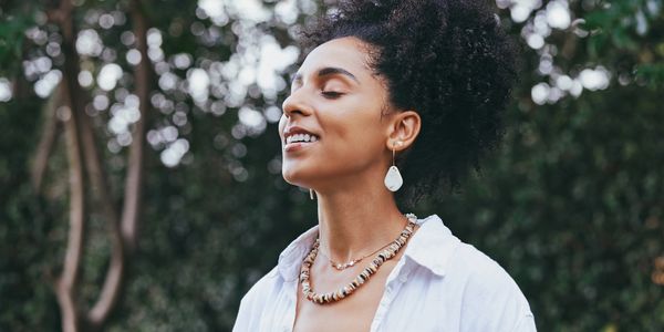 Woman enjoying nature with eyes closed, smiling peacefully.