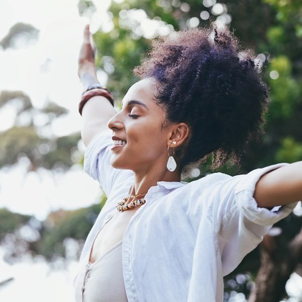 Woman enjoying nature with arms wide open and eyes closed, smiling peacefully.