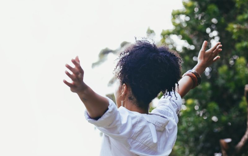 Happy, black woman and freedom with arms out for fresh air, relaxation or breathing in the nature outdoors. African American female enjoying holiday vacation, travel or trip in the countryside