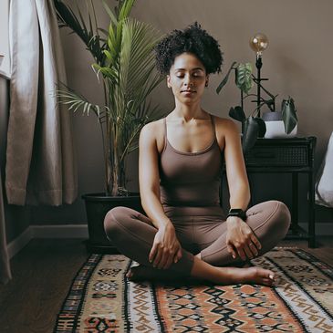 Woman meditating cross-legged in a calm, cozy room, centered and grounded in her practice.