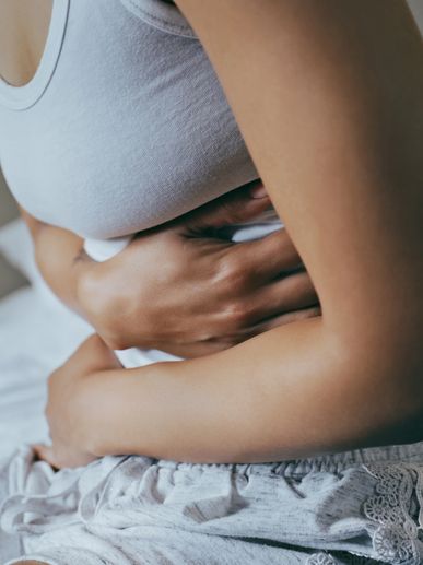 Woman sitting on bed, clutching her stomach in discomfort.