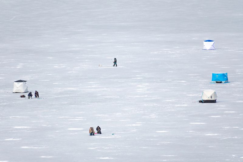 Fishermen fishing on a frozen lake in winter with fishing pole or rod, ice auger and equipment for fishing, portable thermal tents on background