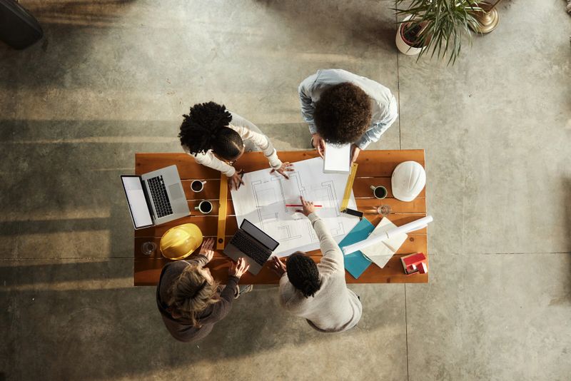 High angle view of team of interior designers cooperating while analyzing plans in the office. Copy space.
