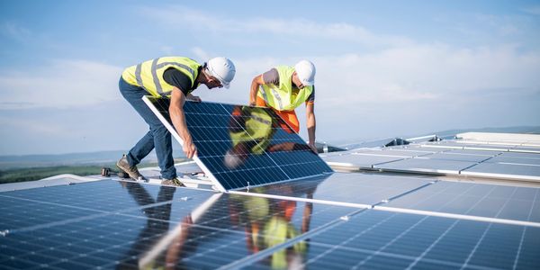 Two workers installing solar panels on a rooftop under a clear sky.