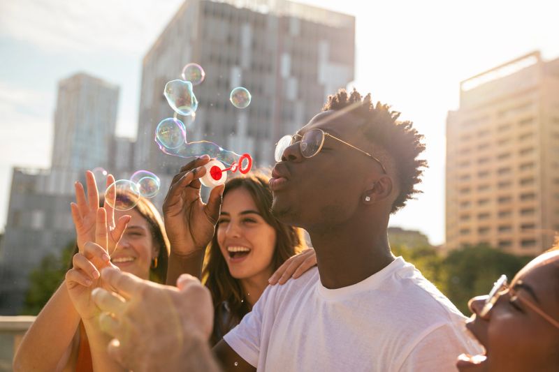 Group of multiracial happy friends having fun with soap bubbles in the city - Cheerful young friends smiling with bubbles on sunny day - Hapiness concept. High quality photo
