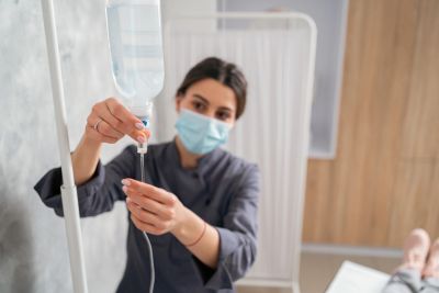 Nurse adjusting an IV drip wearing a face mask.