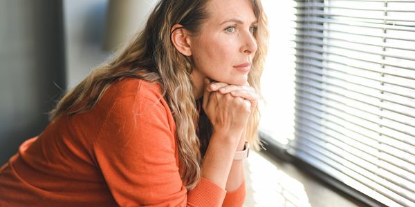 Woman in orange sweater looking thoughtfully out window.