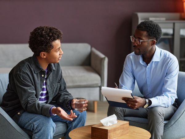 A young man talks to a therapist in a cozy office setting.