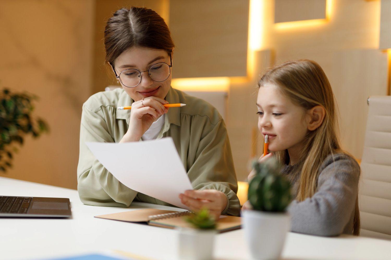 A woman and a girl study together, discussing a document with pencils in hand.