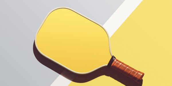 Yellow pickleball paddle resting on a court with yellow and gray colors.