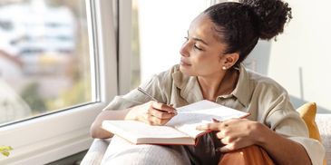 Woman writing in a notebook by the window.