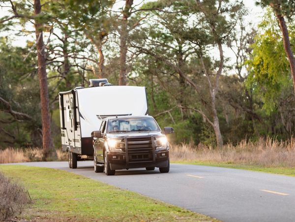 A black pickup truck towing a white camper on a forest road.