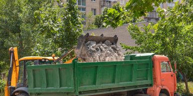 Excavator loading rubble into a green dump truck.