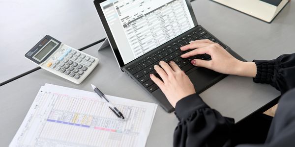 Person working on a laptop with financial documents and calculator nearby.