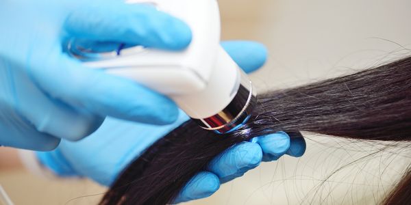 Close-up of a gloved hand using a device on hair strands.
