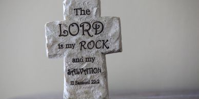 A stone cross with a Bible verse inscription.