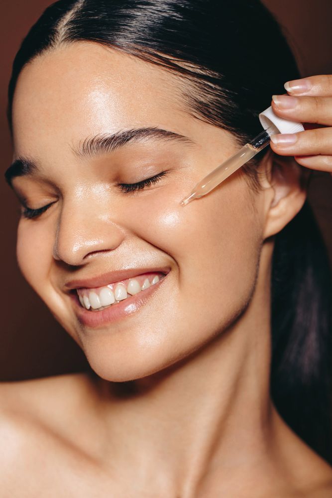 Smiling woman applying facial serum with a dropper for glowing skin.