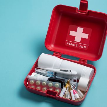 Open red first aid kit with various medical supplies inside on blue background.