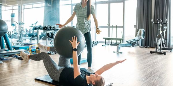 Personal trainer coaching a woman using an exercise ball in a gym.