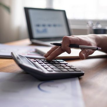 Person using calculator and pen for financial calculations at desk.