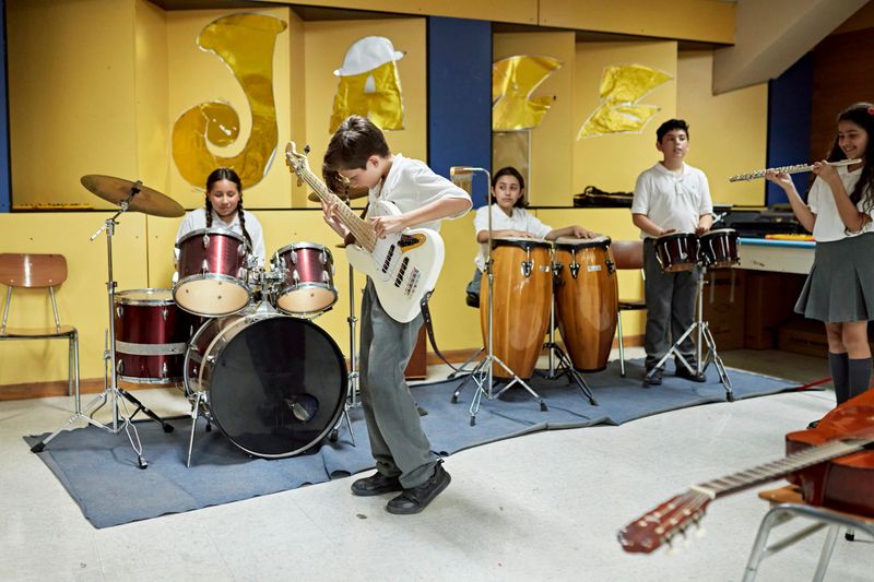 Full length view of Hispanic boys and girls in private school uniforms playing electric guitar, drums, congas, bongos, and flute.
