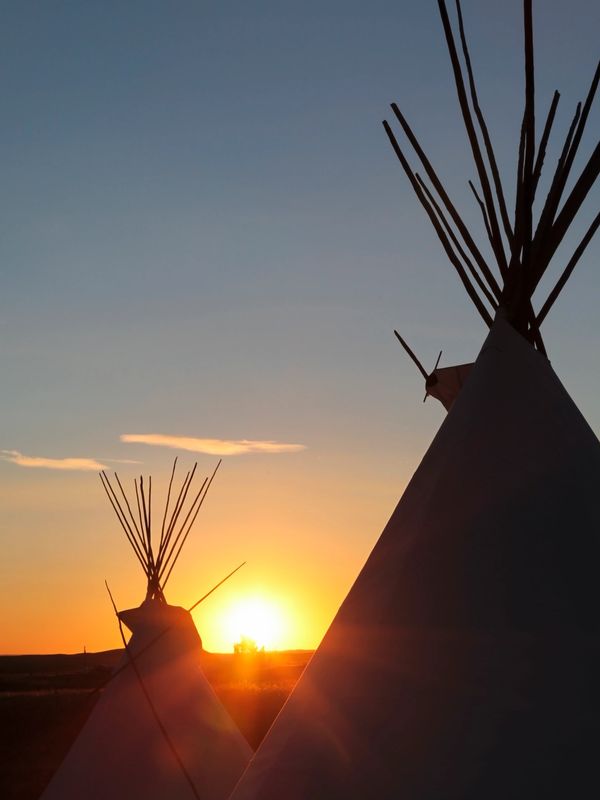 Sunset behind teepees in a serene landscape.