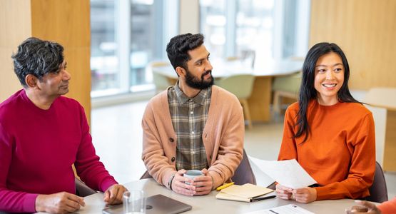Three colleagues in a meeting, smiling and attentive.