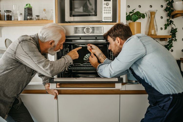 Two men repairing an oven together.