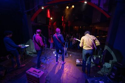 Two musicians playing guitar and bass on stage with colorful lights and energetic crowd.