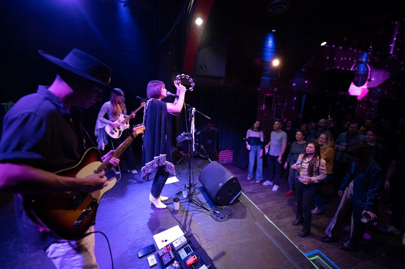 A female fronted rock band performing onstage at a music venue in front of an audience.