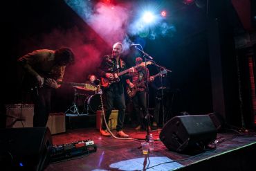 Musician passionately playing acoustic guitar on stage with colorful lights.