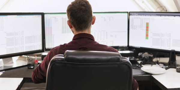 A man working inside the office with three screen
