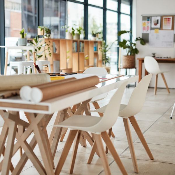 Modern office space with white chairs and a table covered in design plans and samples.
