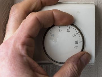 Hand adjusting a wall thermostat dial.