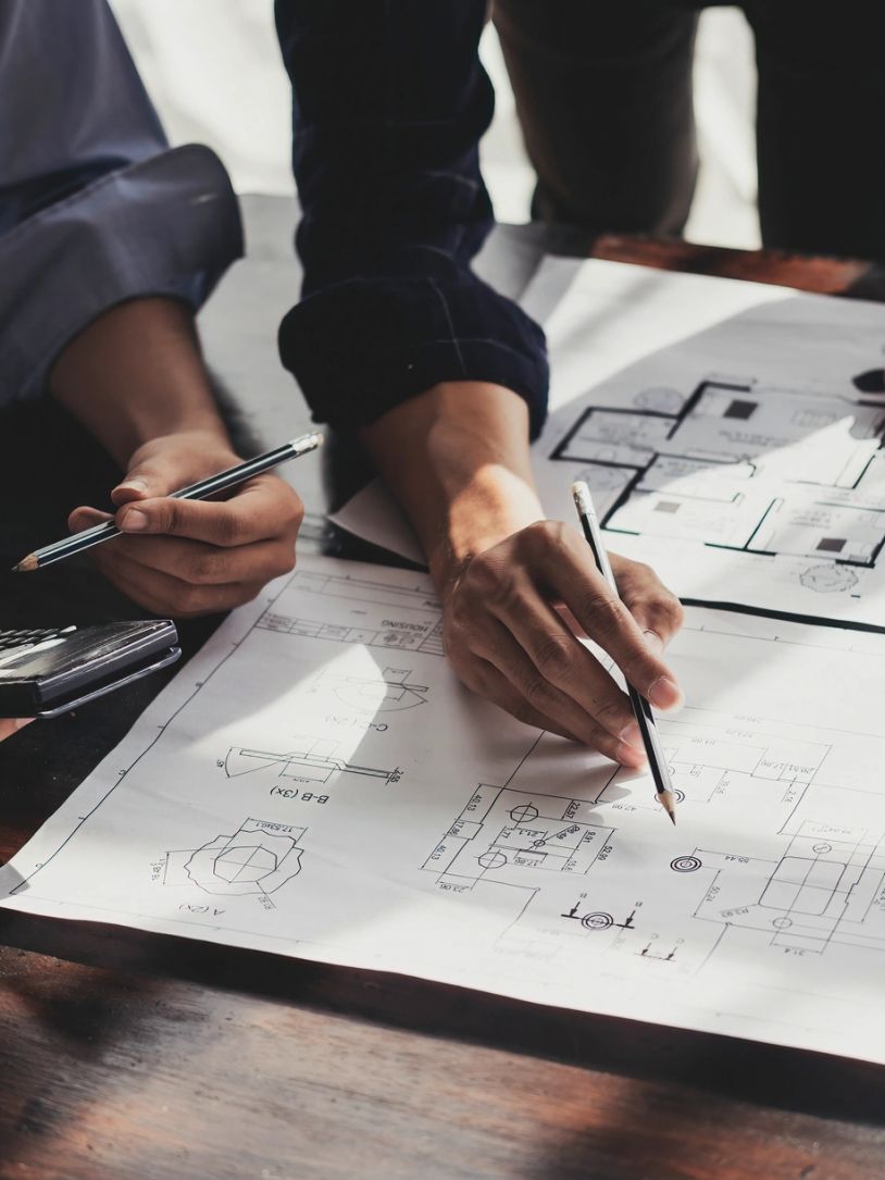 Hands pointing at architectural blueprints with pencils.
