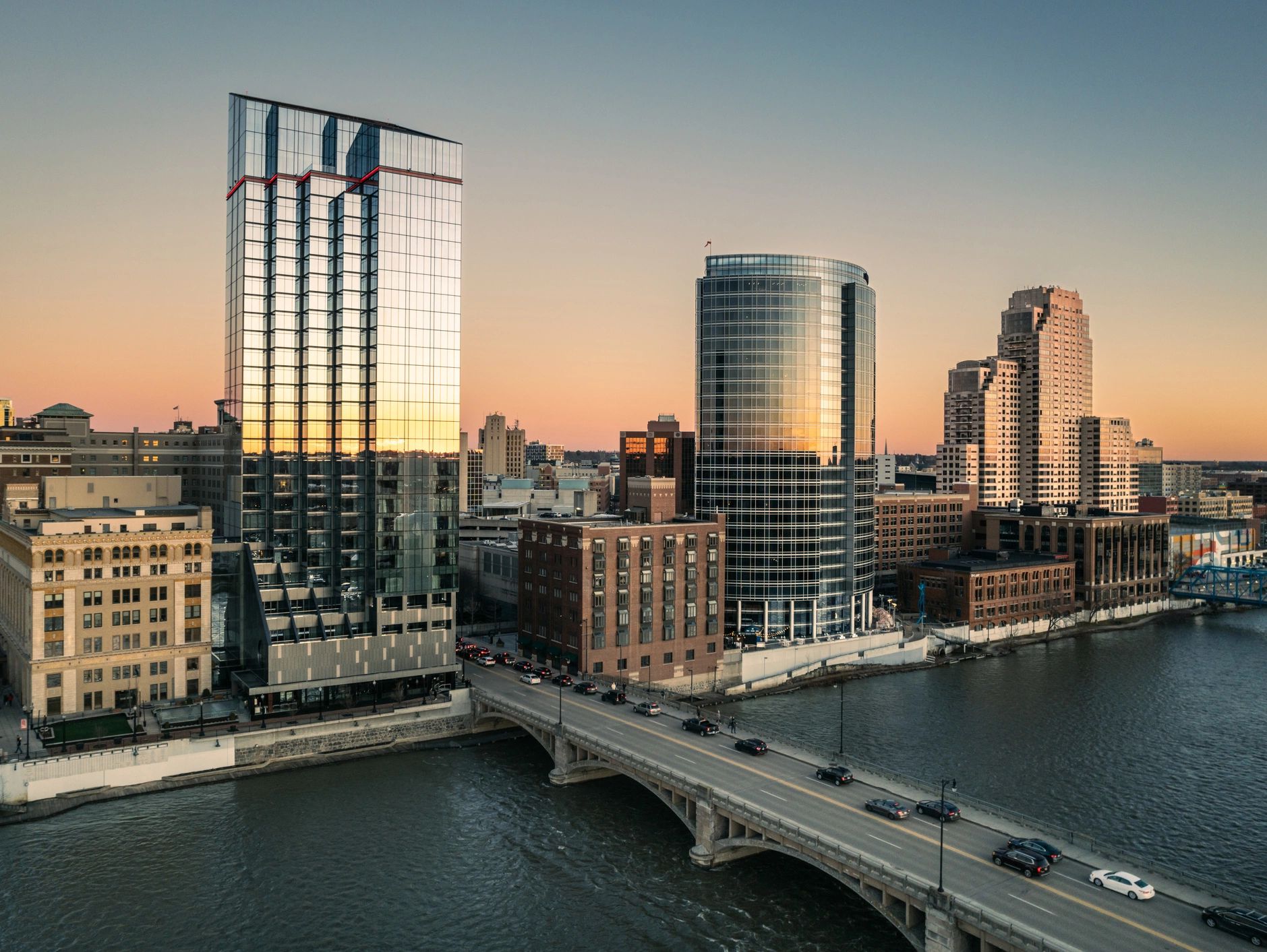 Downtown Grand Rapids, Michigan, featuring a river, bridge, and modern skyline at sunset.