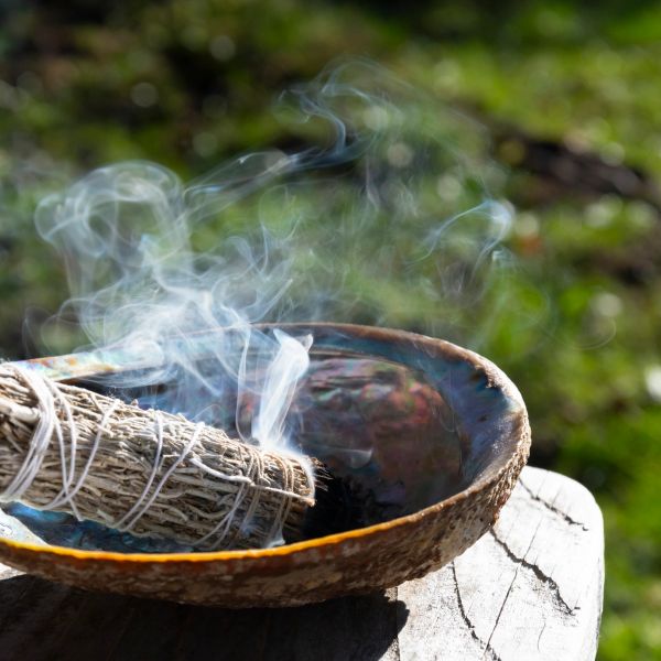 Sage smudge stick releasing smoke in a bowl outdoors.