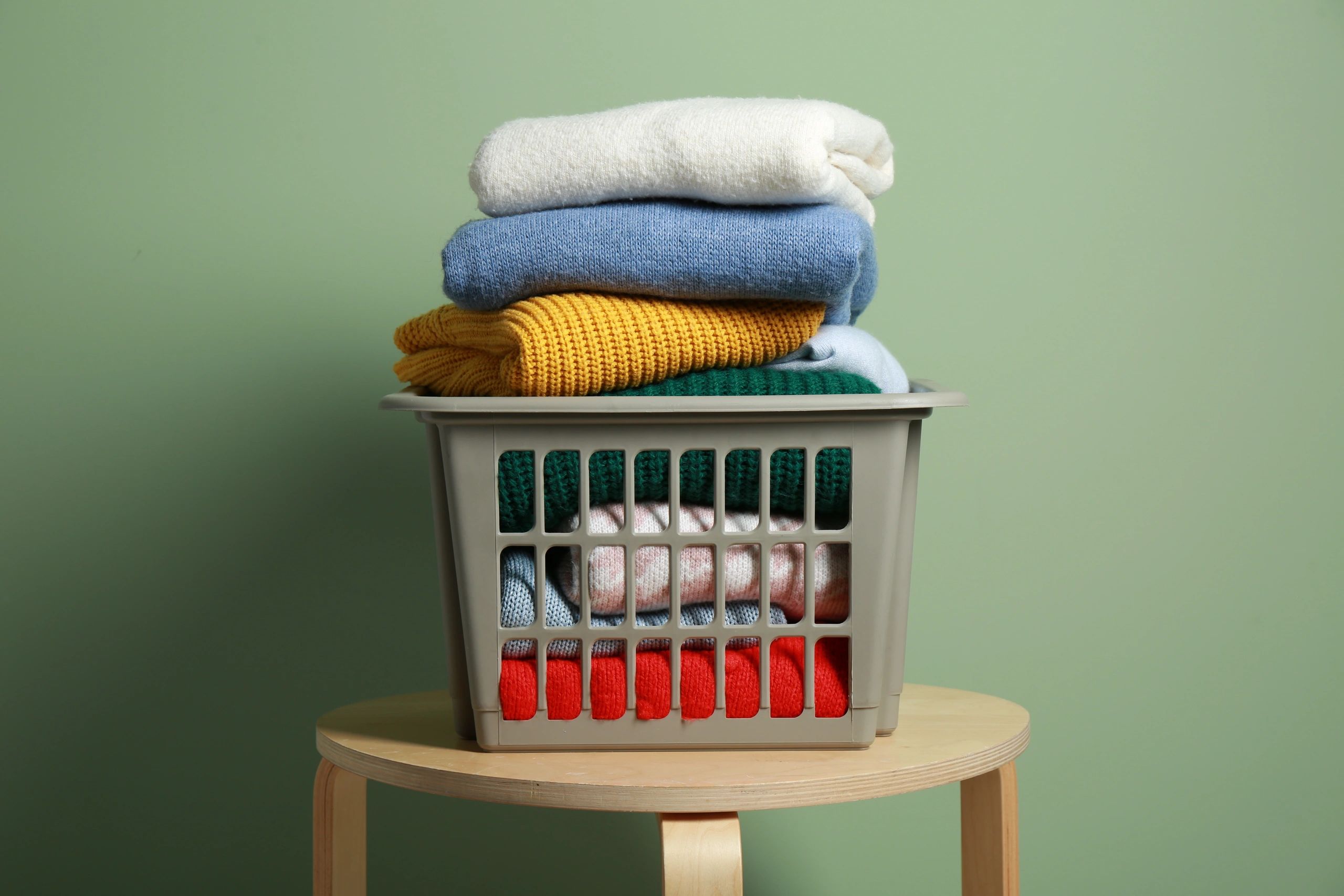 Laundry basket filled with colorful folded sweaters.