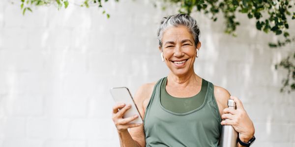 Smiling older woman in workout gear holding a phone and water bottle.