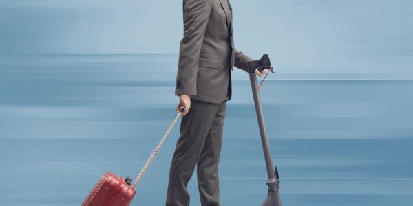 Man in suit with suitcase and scooter.
