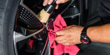 Person cleaning car wheel with brush and cloth.